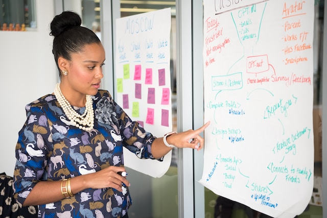 woman standing in front of a large planning sheet, pointing at text
